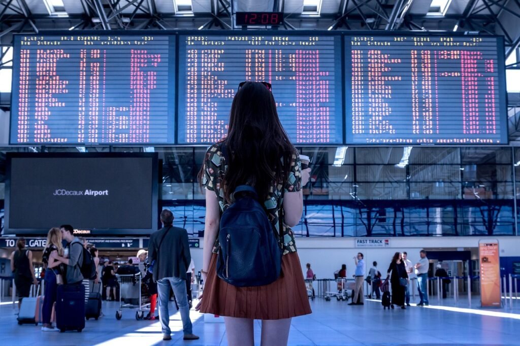 Traveller at an airport departure board, deciding between visitor visa, study and work permit options for Canada